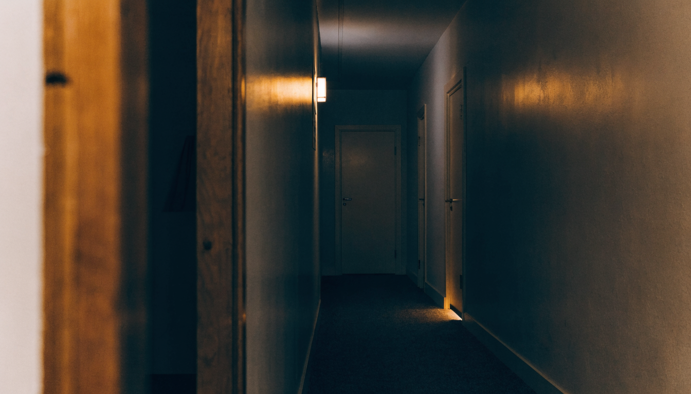 Pasillo de un edificio de viviendas de noche con puertas cerradas y luz cálida, ambiente de silencio tenso entre vecinos